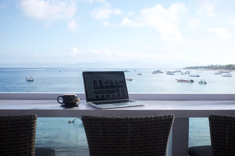 Serene beach view workspace in Bali with a laptop and coffee mug. Perfect for remote work inspiration.