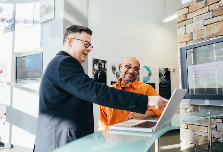 Two businessmen having a lively discussion in a modern office setting, pointing at a laptop screen.